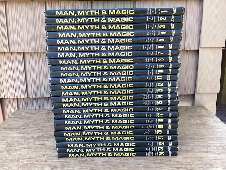 Puede incluir: Una pila de 24 libros titulados "MAN, MYTH & MAGIC" con letras doradas sobre una cubierta negra. Cada libro est&aacute; numerado en el lomo. Los libros est&aacute;n apilados sobre una superficie de madera.