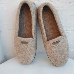May include: A pair of gray wool slippers with blue stitching and a brown leather tag that says "Handmade".