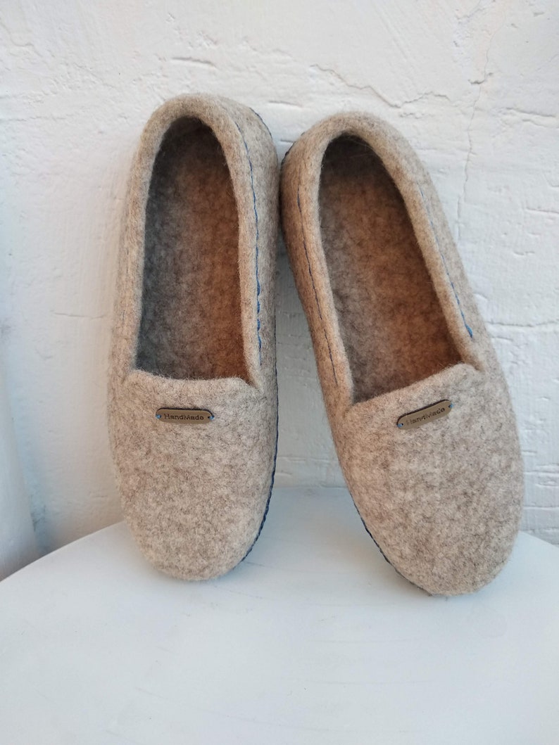 May include: A pair of gray wool slippers with blue stitching and a brown leather tag that says "Handmade".