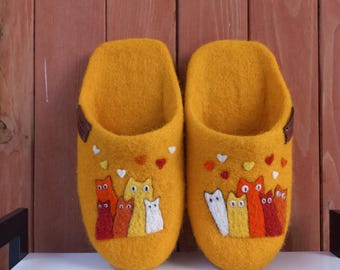 May include: A pair of yellow felt slippers with a design of cats and hearts. The cats are in various shades of orange, yellow, and white.
