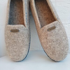 May include: A pair of gray felt slippers with blue stitching and a brown leather tag that says "Handmade".