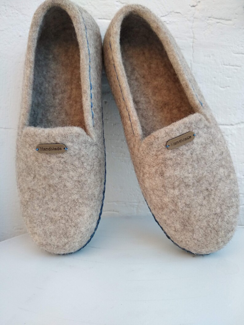May include: A pair of gray felt slippers with blue stitching and a brown leather tag that says "Handmade".