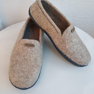 May include: A pair of gray felt slippers with a blue trim and a black sole. The slippers have a label that says "Handmade".
