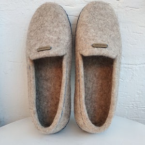 May include: A pair of gray wool slippers with blue stitching and a brown leather tag that says "Handmade".