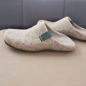 May include: A pair of gray felt slippers with black leather straps and yellow stitching. The slippers have a black rubber sole.