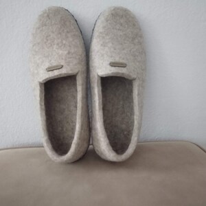 May include: A pair of gray felt slippers with a black rubber sole. The slippers have a simple design and are perfect for keeping your feet warm and cozy.