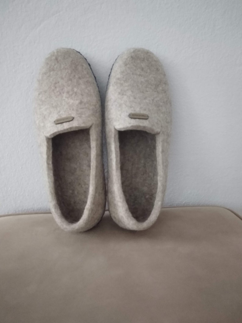 May include: A pair of gray felt slippers with a black rubber sole. The slippers have a simple design and are perfect for keeping your feet warm and cozy.