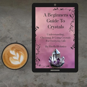 以下が含まれることがあります： 「A Beginners Guide To Crystals」の表紙が映し出されたタブレット。クリスタルのイラストが特徴的。左にはラテアートが施されたコーヒーカップ。背景は質感のあるグレーの表面。
