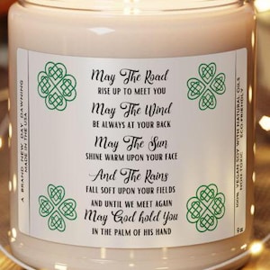 May include: A white candle with a green label that reads "May The Road Rise Up To Meet You May The Wind Be Always At Your Back May The Sun Shine Warm Upon Your Face And The Rains Fall Soft Upon Your Fields And Until We Meet Again May God Hold You In The Palm Of His Hand".