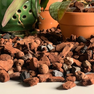 May include: Close-up of a brown orchid bark potting mix with small gray and brown rocks and round clay pellets. The bark is used for growing orchids and other plants.