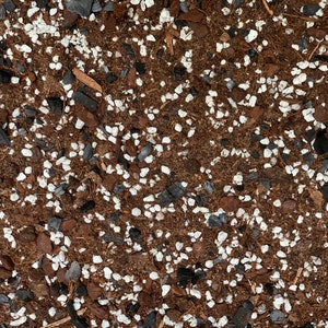 May include: Close-up of a brown soil mixture with white and black pebbles. The soil is used for planting.