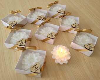 May include: White flower-shaped candles in small white boxes with gold ribbon and a personalized wooden heart tag that says "Morgan & Cliff 09.30.23".