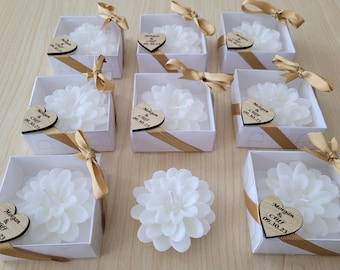 May include: White flower-shaped candles in small white boxes with gold ribbon and a personalized wooden heart tag that says "Morgan & Cliff 09.30.23".
