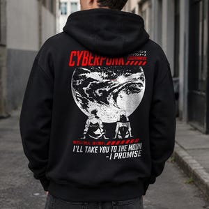 May include: A black hooded sweatshirt featuring a large graphic on the back. The design includes the text CYBERPUNK EDGERUNNERS, a white illustration of a planet, two figures sitting, and the text I'LL TAKE YOU TO THE MOON - I PROMISE.