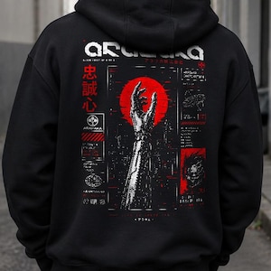 Puede incluir: Una sudadera con capucha negra que presenta un gráfico en la espalda con un sol rojo, un brazo robótico extendido hacia arriba y texto blanco que incluye ARASAKA. El diseño incorpora diagramas técnicos, caracteres japoneses y detalles en rojo.