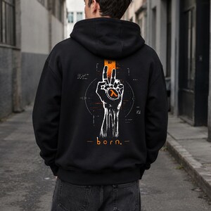 Puede incluir: Una sudadera con capucha negra que presenta un gráfico en la parte posterior. El diseño muestra una mano blanca haciendo el signo de la paz con un símbolo lambda naranja en la palma, rodeado de líneas geométricas y la palabra "born."