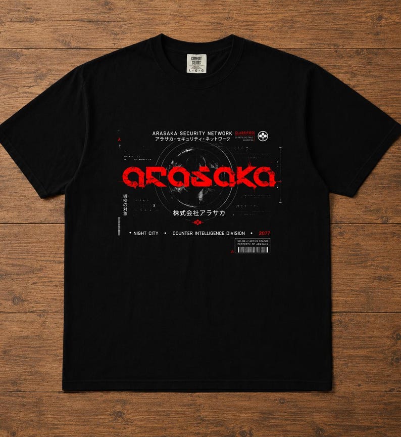 May include: A black short-sleeve t-shirt featuring a graphic print with the red text ARASAKA in a stylized font. The design includes white text reading ARASAKA SECURITY NETWORK, NIGHT CITY, COUNTER INTELLIGENCE DIVISION, and 2077, along with Japanese characters.