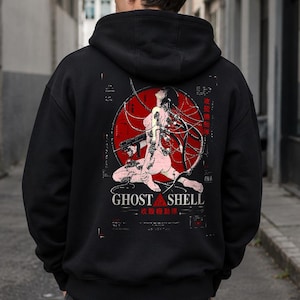 May include: A black hooded sweatshirt featuring a graphic on the back. The design displays a figure connected to cables within a red circle, accompanied by the text GHOST IN THE SHELL and Japanese characters. The hoodie has long sleeves and a hood.