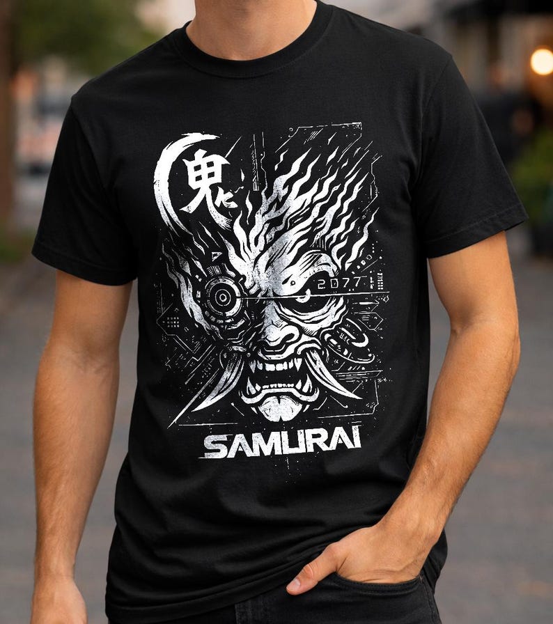 May include: A black short-sleeved t-shirt featuring a white graphic print of a stylized robotic samurai mask. The design includes the Japanese kanji for demon, the text 2077, and the word SAMURAI printed in a bold, sans-serif font at the bottom.