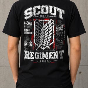 Könnte beinhalten: Ein schwarzes Kurzarm-T-Shirt mit einer großen Grafik auf der Rückseite. Das Design enthält den Text SCOUT REGIMENT, ein zentrales Flügel-Emblem sowie kleinere Felder mit dem Text TITAN RESEARCH, FOR A BRIGHTER TOMORROW und WINGS OF FREEDOM.