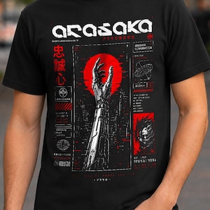 May include: A black t-shirt featuring a graphic print of a robotic arm reaching toward a red circle. The design includes the text ARASAKA, Japanese characters, and technical diagrams in white and red ink, creating a detailed, industrial-style aesthetic.