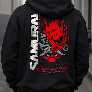 Puede incluir: Una sudadera con capucha negra que presenta un gráfico en la parte posterior con la palabra SAMURAI en texto vertical blanco. El diseño incluye una máscara oni robótica roja y blanca con llamas y el texto rojo REUNION TOUR 2020 abajo.