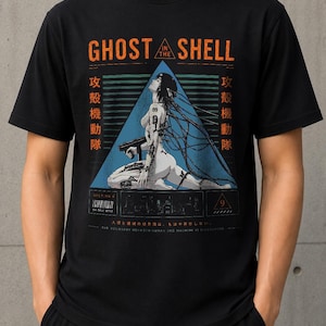 Könnte beinhalten: Ein schwarzes Kurzarm-T-Shirt mit einem Ghost in the Shell-Grafikdruck. Das Motiv zeigt einen Cyborg mit Kabeln, ein blaues Dreieck, japanische Schriftzeichen und den Schriftzug Ghost in the Shell. Es enthält einen Barcode und den Text The boundary between human and machine is dissolving.