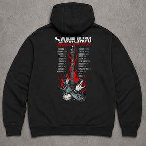 May include: A black hooded sweatshirt featuring a graphic on the back with the text SAMURAI REUNION TOUR 2020. The design includes a central electric guitar surrounded by red flames and a robotic hand, flanked by two columns of city names.
