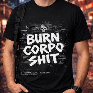 Puede incluir: Camiseta negra con la frase "BURN CORPO SHIT" en letras blancas. El dise&ntilde;o incluye una calavera con auriculares y efectos de glitch. El texto "ILLEGAL BROADCAST" est&aacute; impreso en la parte inferior.