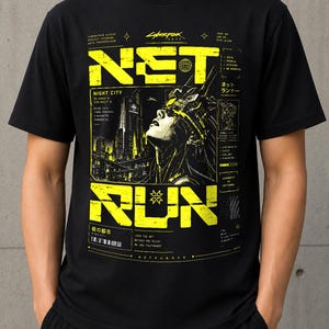 May include: A black short-sleeve t-shirt featuring a yellow graphic print with the text "NET RUN" and "CYBERPUNK 2077". The design includes a futuristic cityscape, a character wearing a headset, and various technical data labels and symbols.