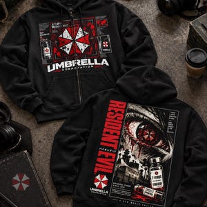 Może przedstawiać: Czarna bluza z kapturem zapinana na zamek, z czerwono-białym logo Umbrella Corporation na piersi oraz japońskim tekstem. Z tyłu znajduje się duża grafika ludzkiego oka z czerwoną tęczówką, fiolka z wirusem T oraz napis Resident Evil.
