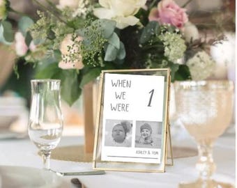 May include: Gold framed table number with black and white photos of a baby boy and girl. The text reads "When we were 1" and "Ashley & Tom".