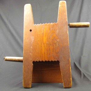 May include: A wooden butter churn with a handle on the side. The churn has a series of grooves on the front and a small hole on the side.
