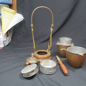 May include: A vintage copper coffee percolator with a brass handle and a wooden stirring stick. The percolator is disassembled and laid out on a black surface.