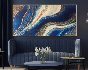 May include: Abstract painting with blue and gold swirls on a canvas. The painting is framed in gold and hangs on a dark blue wall above a blue velvet sofa.