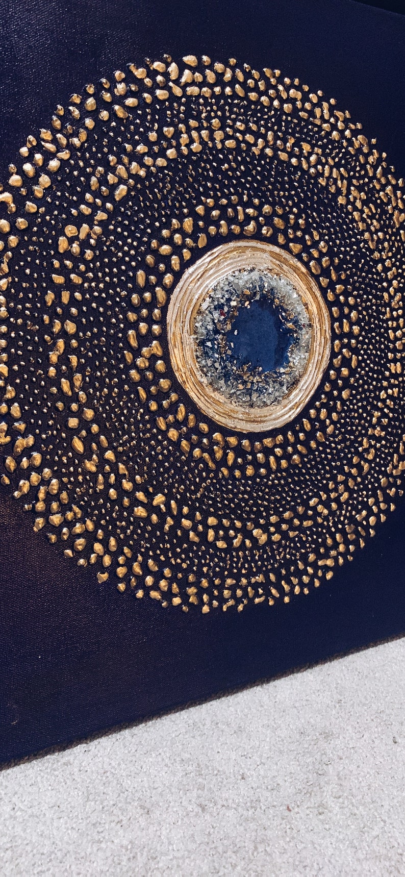 May include: A circular abstract painting with a gold and white center and a dark blue background. The center is surrounded by a ring of gold dots.