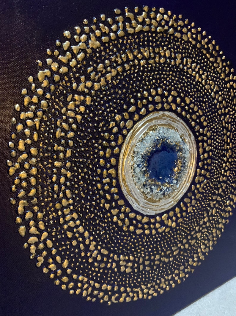May include: A navy blue canvas painting with a gold and white circular design. The center of the circle features a blue and white agate stone.