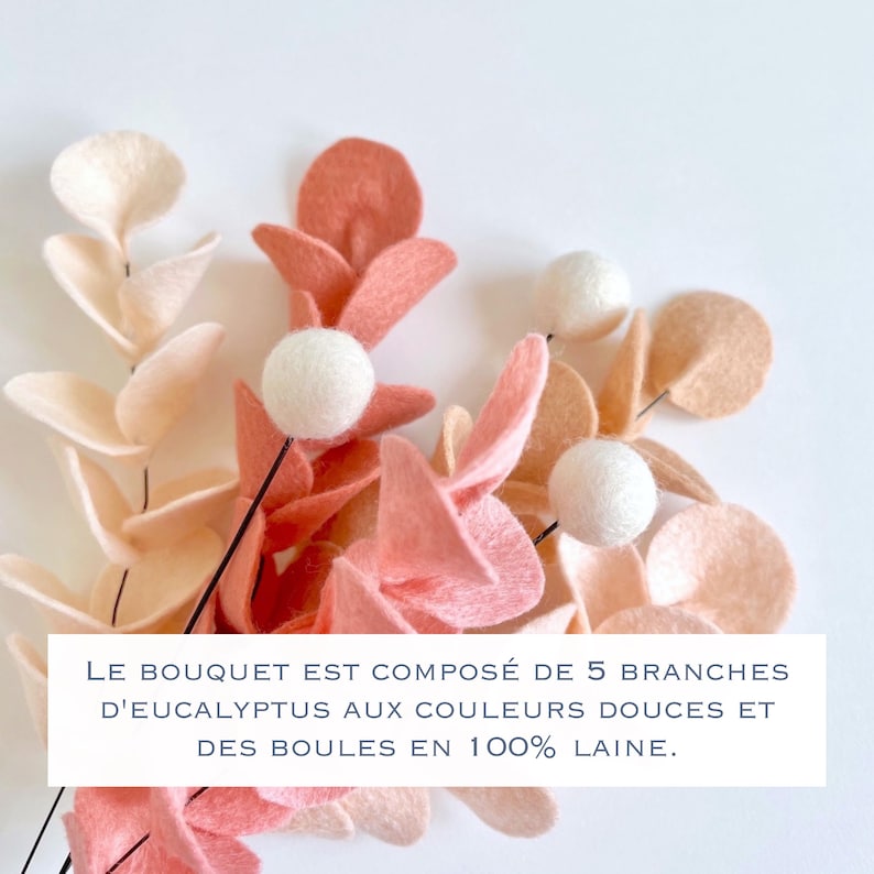 Pode incluir: Um buqu&ecirc; de cinco ramos de eucalipto de feltro em tons suaves de creme, p&ecirc;ssego e coral, acentuado com bolas de l&atilde; branca. O texto na imagem diz: LE BOUQUET EST COMPOS&Eacute; DE 5 BRANCHES D'EUCALYPTUS AUX COULEURS DOUCES ET DES BOULES EN 100% LAINE.