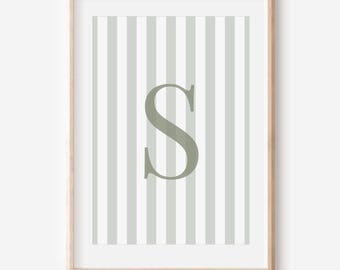 May include: A framed print featuring a large, sage green letter "S" centered on a background of vertical stripes in white and a muted green. The artwork is encased in a light wood frame, suitable for home decor.