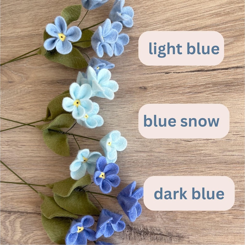 May include: Handmade felt flowers in light blue, blue snow, and dark blue. Each flower has a yellow center and green leaves. The image includes text labels: "light blue", "blue snow", and "dark blue".