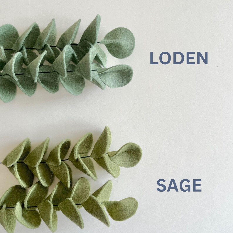 May include: Two felt leaf garlands arranged horizontally. The top garland is light green with the text LODEN printed to its right. The bottom garland is a darker olive green with the text SAGE printed to its right. Both feature rounded leaves.