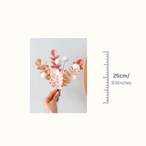 Pode incluir: Um buqu&ecirc; de hastes artificiais com folhas arredondadas em tons de rosa, p&ecirc;ssego e creme, acentuado com pequenas esferas brancas. As hastes medem 25 cm de altura total, conforme indicado pelo gr&aacute;fico de escala adjacente.