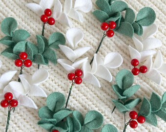 May include: A collection of felt craft stems featuring clusters of small, round, glossy red berries paired with either white or sage green felt leaves. Each stem is constructed with a thin wire base, showcasing a mix of foliage colors.