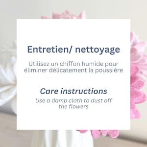 May include: A white square card featuring dark blue text that reads Entretien/ nettoyage, Utilisez un chiffon humide pour &eacute;liminer d&eacute;licatement la poussi&egrave;re, Care instructions, and Use a damp cloth to dust off the flowers, with pink and white felt flowers.