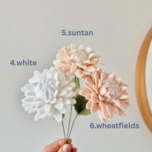 May include: Three felt flowers on thin green stems. The flower labeled 4.white is white, 5.suntan is a light peach, and 6.wheatfields is a soft tan. Each flower has multiple layers of rounded petals and a textured center, creating a full bloom.
