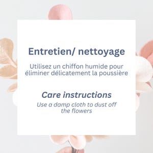 Pode incluir: Um cart&atilde;o quadrado branco com texto azul escuro lendo Entretien/ nettoyage, Utilisez un chiffon humide pour &eacute;liminer d&eacute;licatement la poussi&egrave;re, Care instructions, Use a damp cloth to dust off the flowers, contra p&eacute;talas de feltro rosa.