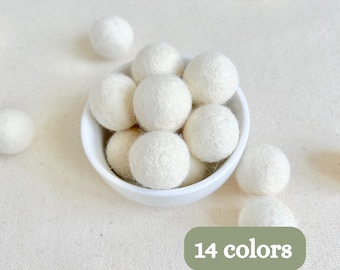 May include: A small white bowl filled with several round, textured white felt balls. Additional white felt balls are scattered around the bowl. A green rectangular graphic in the corner displays the white text 14 colors.