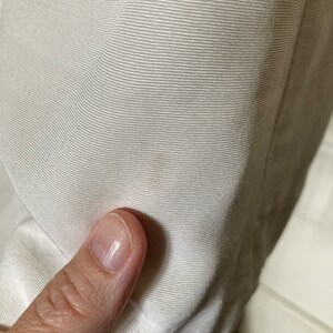 May include: A close-up view of off-white fabric featuring a fine, horizontal ribbed texture. The material displays a consistent, tightly woven pattern with subtle light and shadow variations across the surface, highlighting the linear weave.