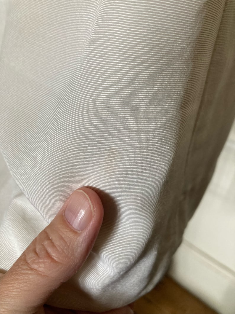 May include: A close-up view of off-white fabric featuring a fine, horizontal ribbed texture. The material displays a consistent, tightly woven pattern with subtle light and shadow variations across the surface, highlighting the linear weave.