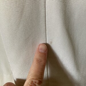 May include: A light beige fabric with a fine horizontal ribbed texture and a vertical seam running down the center. A small, faint brown spot is visible on the right side of the seam, indicating a minor imperfection in the material surface.